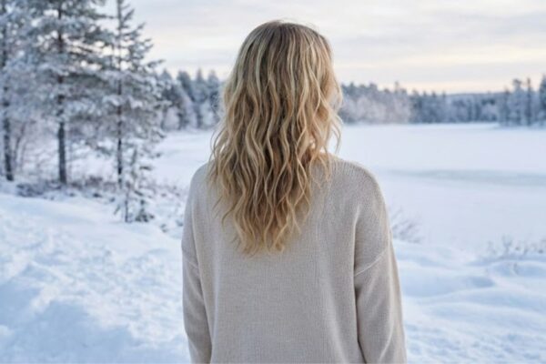 Rear view of blonde hair with soft, deconstructed beach waves styling against a blurred snowy winter landscape, highlighting natural texture.