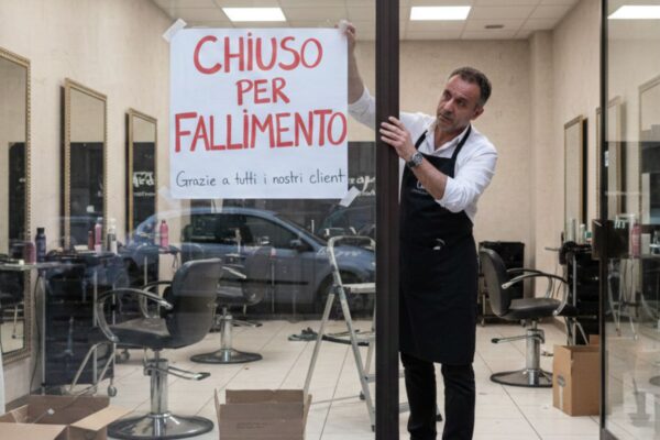 Parrucchiere sconfortato appende il cartello "Chiuso per fallimento" sulla vetrina del suo salone di bellezza, simbolo della crisi del settore.