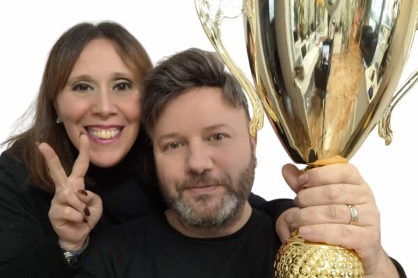 Un uomo e una donna sorridenti, rappresentanti di Maison Miracle, festeggiano un traguardo tenendo in mano un grande trofeo dorato.