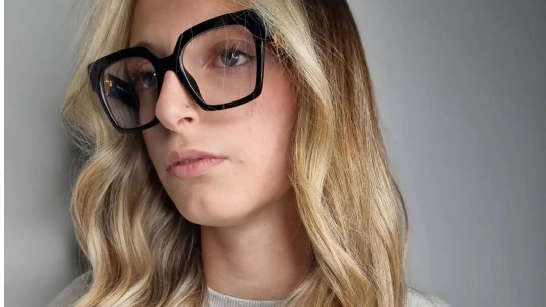 Primo piano di una modella con capelli lunghi e mossi che mostrano la colorazione Coconut Blonde: radici scure cenere che sfumano in lunghezze biondo freddo chiarissimo.