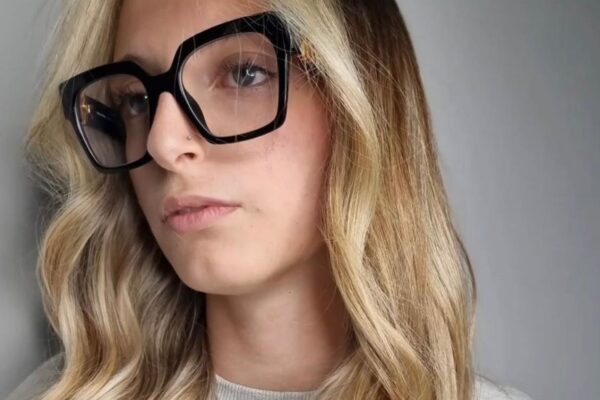 Primo piano di una modella con capelli lunghi e mossi che mostrano la colorazione Coconut Blonde: radici scure cenere che sfumano in lunghezze biondo freddo chiarissimo.