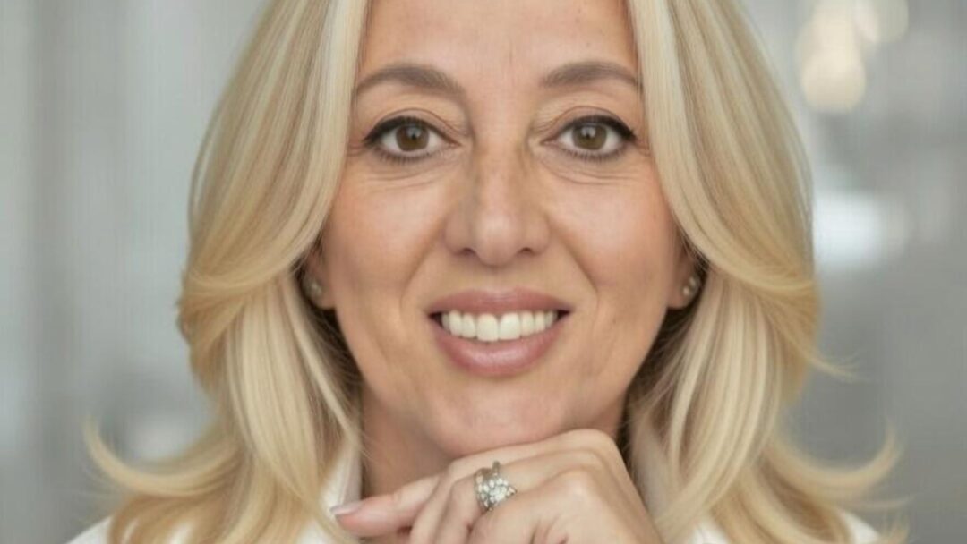 Primo piano professionale di Paola D'andria, sorridente con la mano sotto il mento.