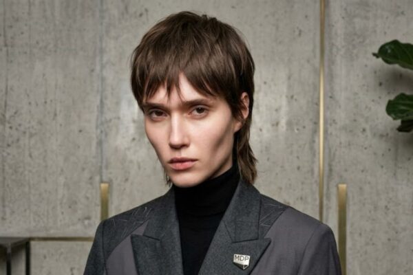 Modella con taglio corto sfilato Trixie Cut e giacca grigia con spilla MDP.