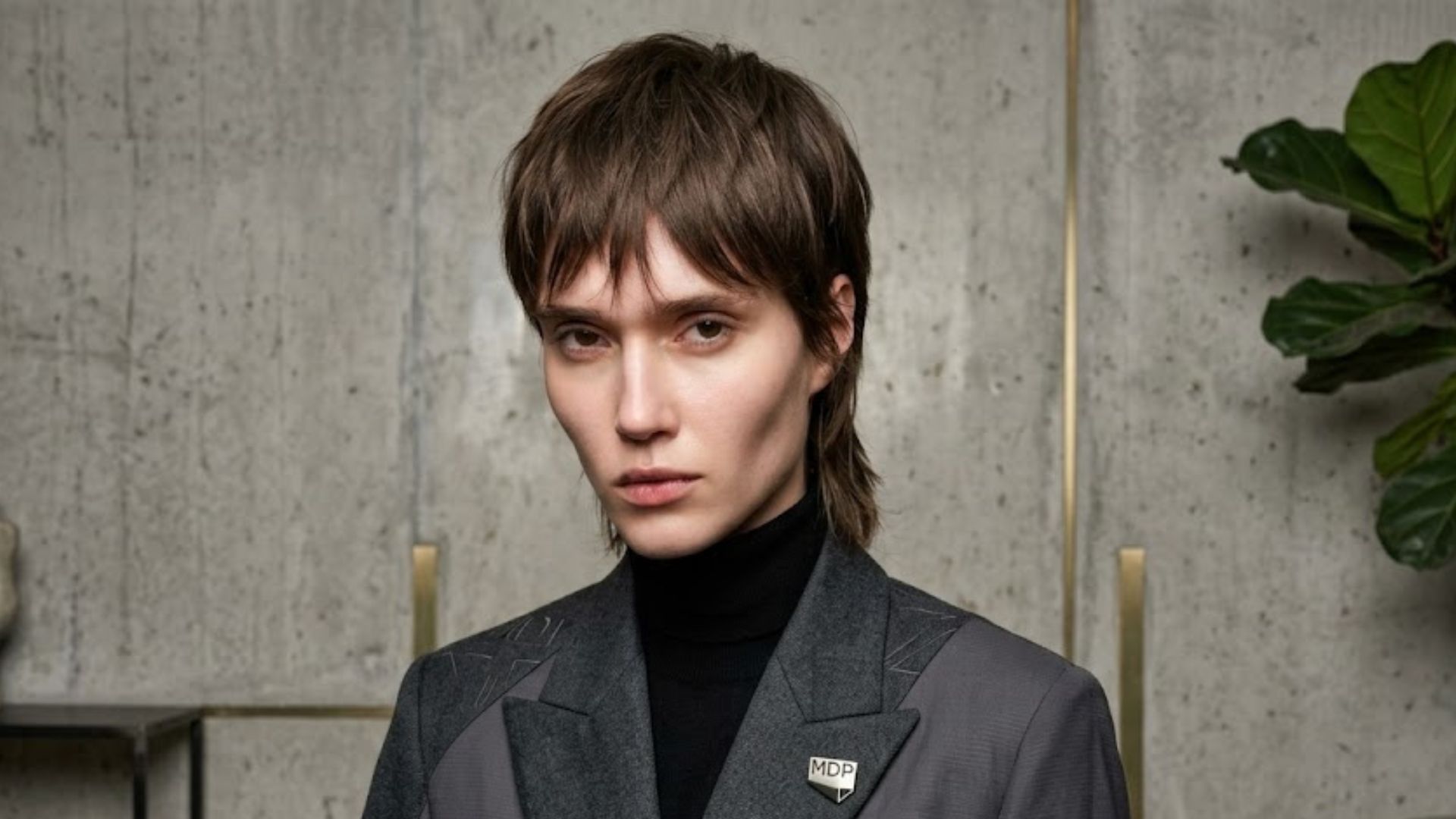 Modella con taglio corto sfilato Trixie Cut e giacca grigia con spilla MDP.