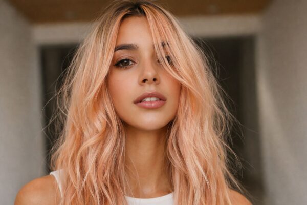 Professional model showcasing pastel peach blonde hair with soft waves, Spring 2026 hair color trend.