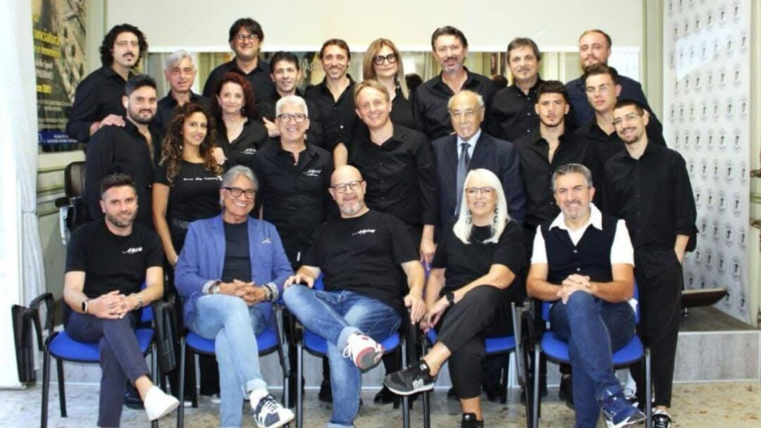 Un numeroso gruppo di parrucchieri e professionisti del settore dell'acconciatura in posa per una foto istituzionale in accademia.