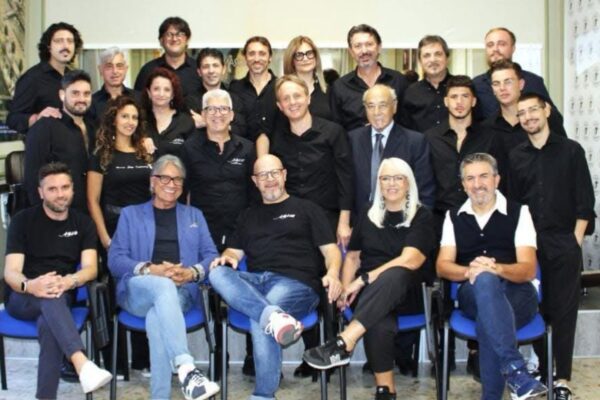 Un numeroso gruppo di parrucchieri e professionisti del settore dell'acconciatura in posa per una foto istituzionale in accademia.