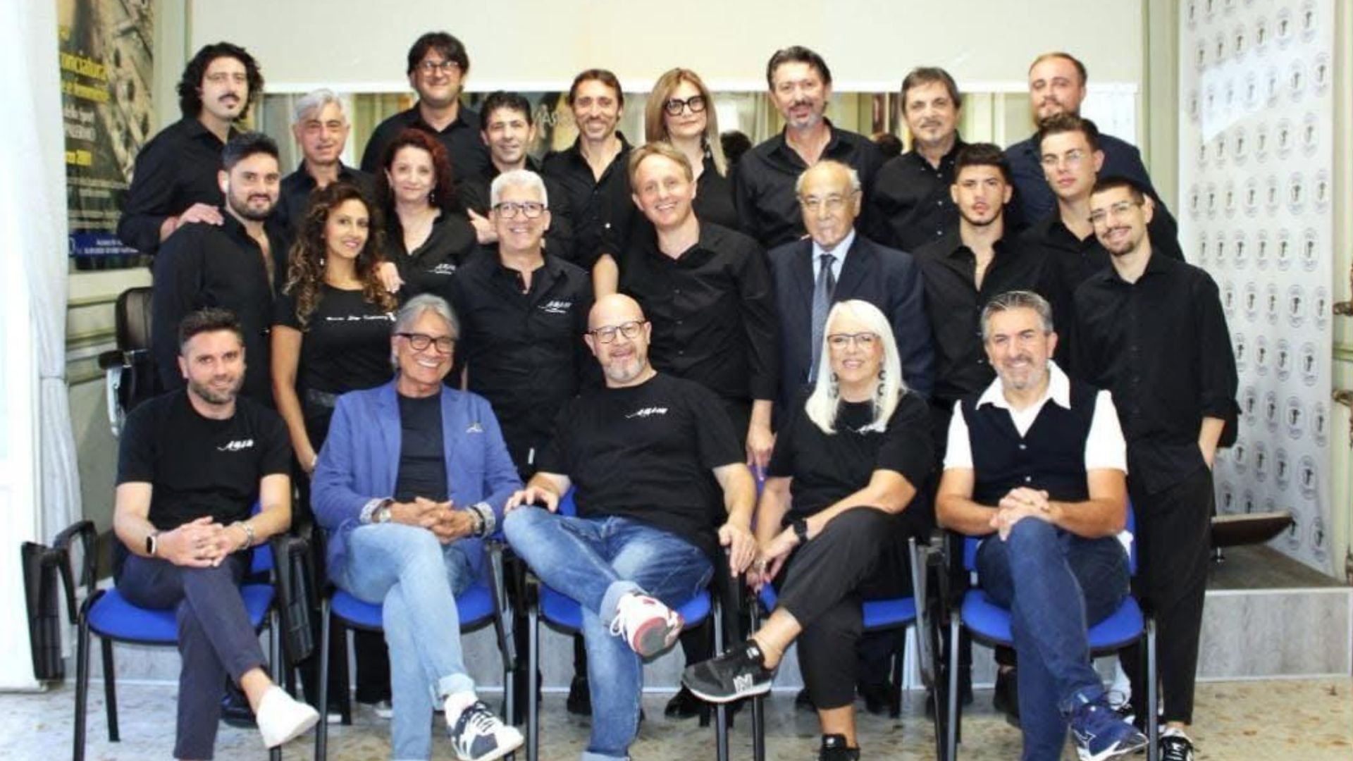 Un numeroso gruppo di parrucchieri e professionisti del settore dell'acconciatura in posa per una foto istituzionale in accademia.