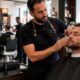 Barbiere professionista applica un trattamento viso a un cliente in un barber shop moderno, con prodotto BB Skill sul banco.