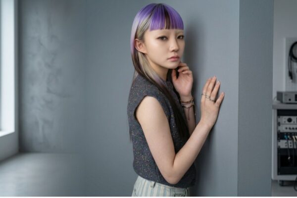 Modella con look capelli Purple Black Mode Design, taglio lungo liscio con micro-frangia viola e biondo platino, in posa di profilo in uno studio fotografico moderno su sfondo grigio.