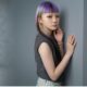 Modella con look capelli Purple Black Mode Design, taglio lungo liscio con micro-frangia viola e biondo platino, in posa di profilo in uno studio fotografico moderno su sfondo grigio.