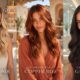 Banner orizzontale editoriale con tre ritratti affiancati della stessa donna che mostrano tre tendenze colore capelli estate: a sinistra Nude Butter Blonde in salone luminoso, al centro Terracotta Copper Red su patio mediterraneo, a destra Espresso Glacé in interno elegante. Ogni look mette in evidenza texture, lucentezza e personalità del colore.