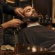 Barbiere professionista esegue un trattamento barba premium su un cliente in un barber shop italiano di lusso.