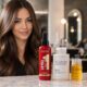 Donna con capelli castani lunghi, lisci e luminosi in un salone moderno, con prodotti Revlon Professional Uniq One e Olaplex in primo piano su un piano in marmo.