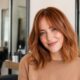 Modella in salone con capelli color rame soft copper, taglio long bob e frangia a tendina.