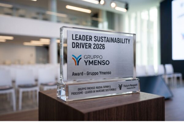 Trofeo in vetro e metallo del premio Leader Sustainability Driver 2026 assegnato al Gruppo Ymenso, posizionato su un piedistallo in legno con una sala conferenze sfocata sullo sfondo.