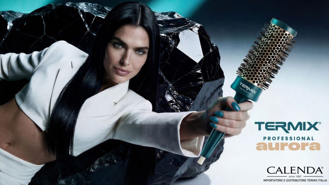 Modella con capelli lisci scuri regge una spazzola termica Termix Aurora Professional con manico verde acqua e setole dorate, sfondo scuro con roccia effetto specchio, logo Calenda importatore ufficiale