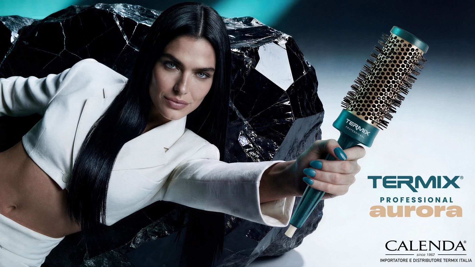 Modella con capelli lisci scuri regge una spazzola termica Termix Aurora Professional con manico verde acqua e setole dorate, sfondo scuro con roccia effetto specchio, logo Calenda importatore ufficiale