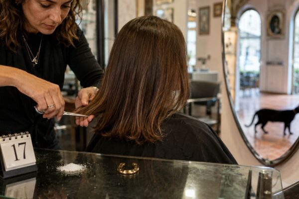 Parrucchiera taglia i capelli a una cliente in salone con calendario 17, sale, ferro di cavallo e gatto nero sullo sfondo.
