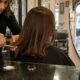 Parrucchiera taglia i capelli a una cliente in salone con calendario 17, sale, ferro di cavallo e gatto nero sullo sfondo.