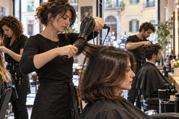Stylist giving a round-brush blow-dry in a busy Italian neighbourhood salon