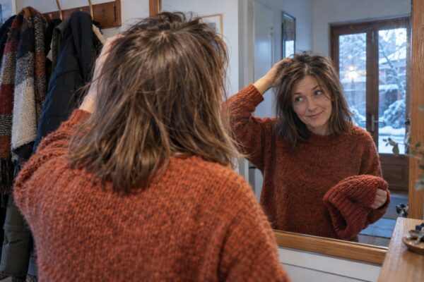 Cliente osserva allo specchio i capelli fini dopo aver tolto il berretto invernale.