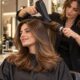 Parrucchiera realizza una piega professionale su capelli castani lunghi con phon e spazzola, salone contemporaneo