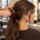 Stylist sistema un fiocco in velluto in una coda bassa su capelli castani. Immagine generata da AI.
