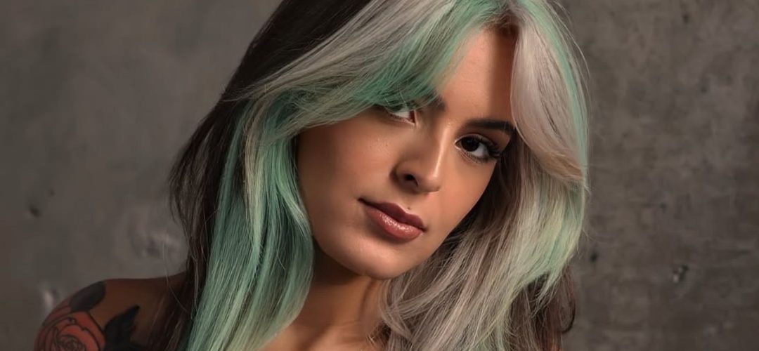 Donna con capelli lunghi color menta, cioccolato e biondo freddo, taglio scalato con curtain bangs, su sfondo grigio.