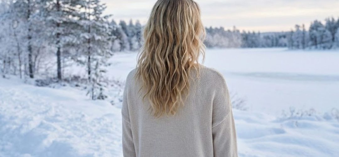 Rear view of blonde hair with soft, deconstructed beach waves styling against a blurred snowy winter landscape, highlighting natural texture.