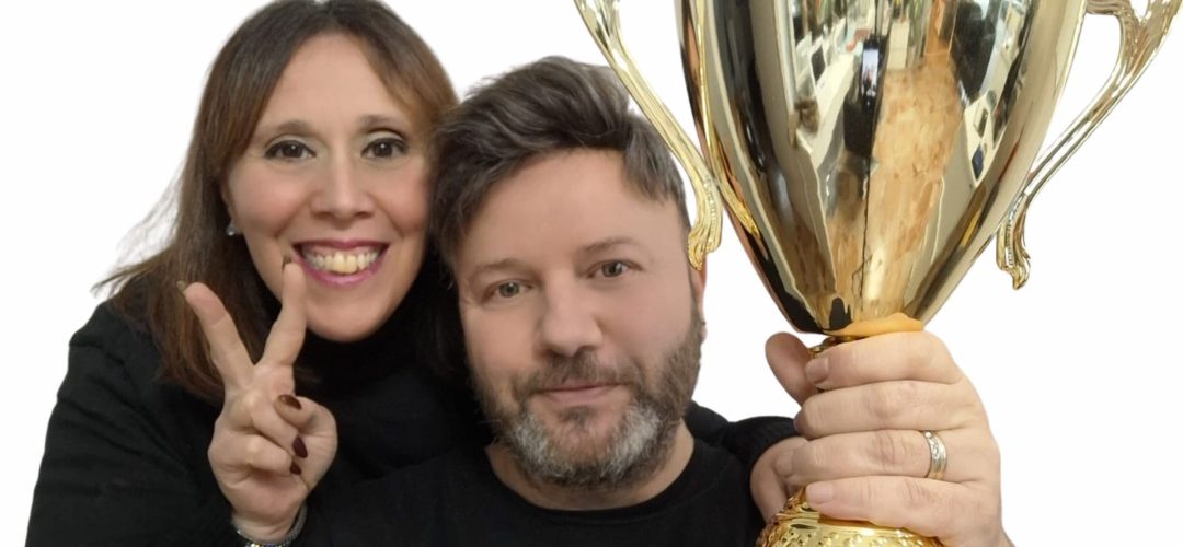 Un uomo e una donna sorridenti, rappresentanti di Maison Miracle, festeggiano un traguardo tenendo in mano un grande trofeo dorato.
