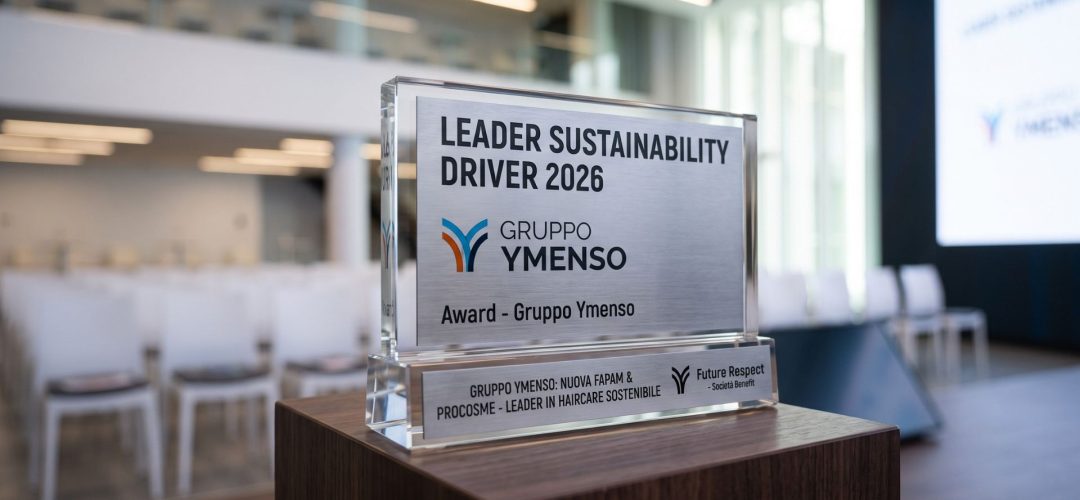 Trofeo in vetro e metallo del premio Leader Sustainability Driver 2026 assegnato al Gruppo Ymenso, posizionato su un piedistallo in legno con una sala conferenze sfocata sullo sfondo.