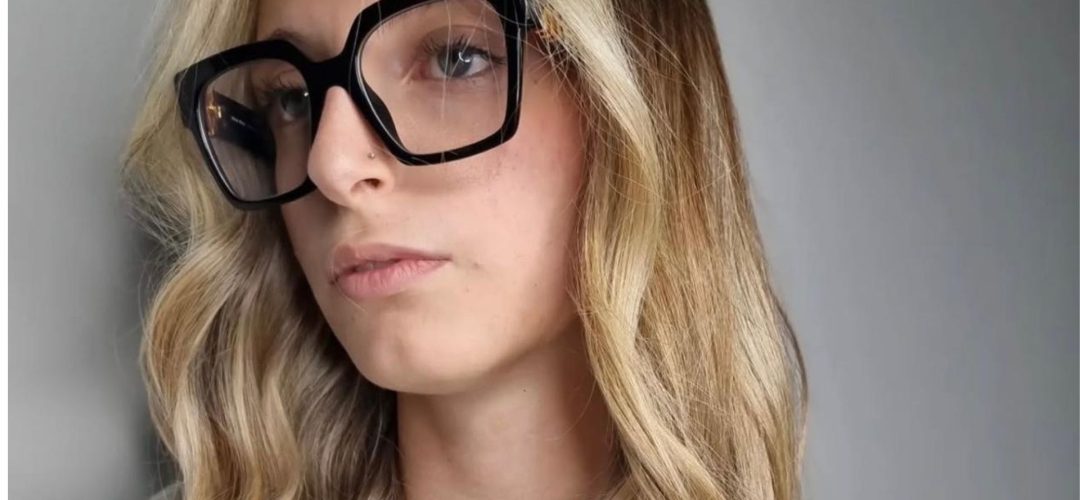Primo piano di una modella con capelli lunghi e mossi che mostrano la colorazione Coconut Blonde: radici scure cenere che sfumano in lunghezze biondo freddo chiarissimo.