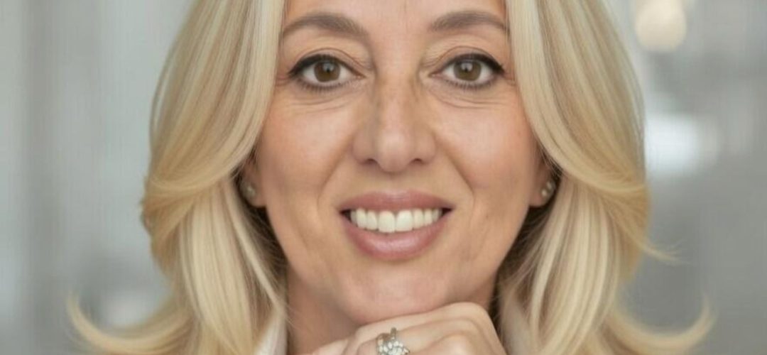 Primo piano professionale di Paola D'andria, sorridente con la mano sotto il mento.