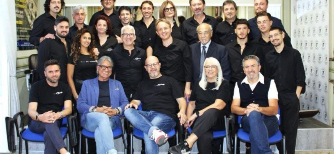 Un numeroso gruppo di parrucchieri e professionisti del settore dell'acconciatura in posa per una foto istituzionale in accademia.