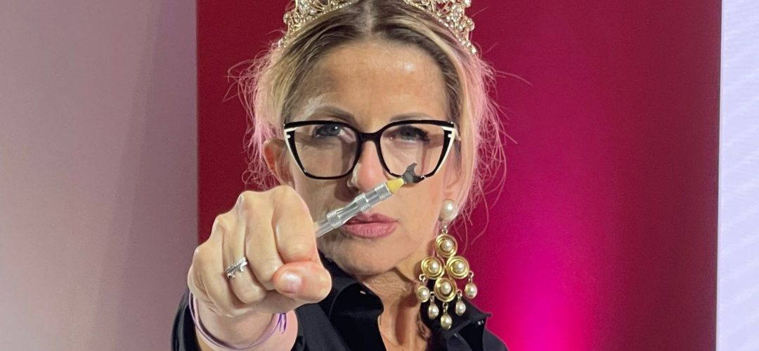 Hairstylist con corona e occhiali punta verso la camera uno strumento tecnico per capelli durante una dimostrazione.